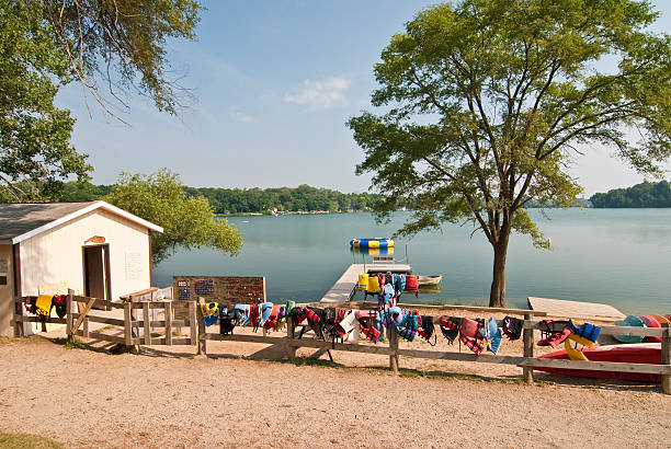 View of beach at Summer Camp with boat house, changing room, wooden fence with life jackets and life preservers hanging, trees, lake, boats
Photo courtesy of pixabay
