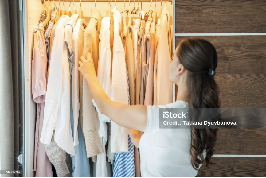 young woman standing in wardrobe and choosing outfit from hangers 

