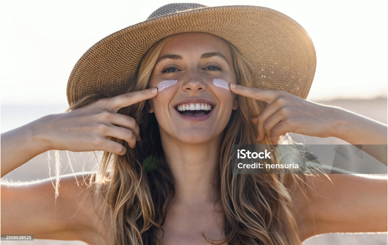 Smiling woman applying sunscreen on her face.